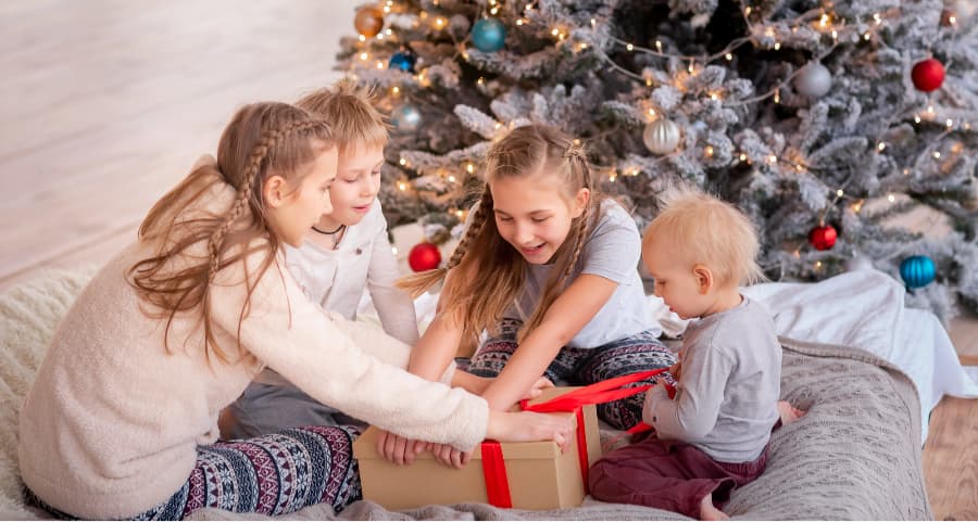 Kids opening a gift beside a Christmas tree.